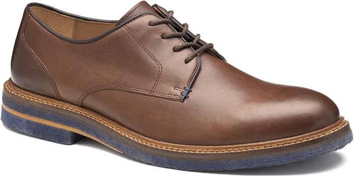 Medium brown leather plain-toe oxford shoe shown from a three-quarter front angle. Features dark brown laces, tan leather insole, contrast navy blue outsole, and visible blue accent stitching near the toe.