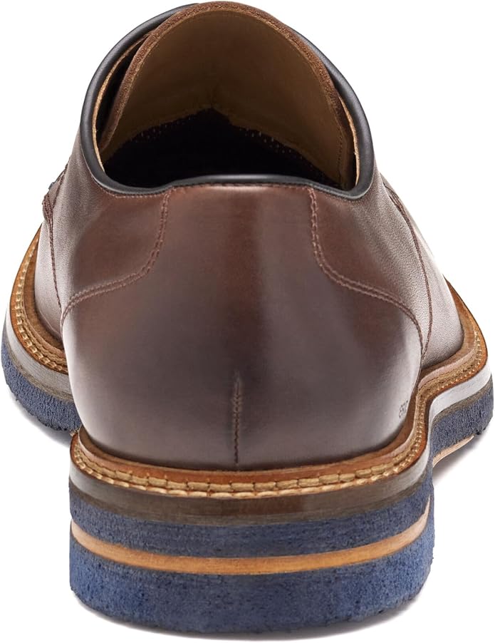 Rear view of a brown leather oxford dress shoe with a layered sole featuring tan, white, and navy blue sections. Visible heel counter, tan topstitching along the welt, and a dark interior lining.